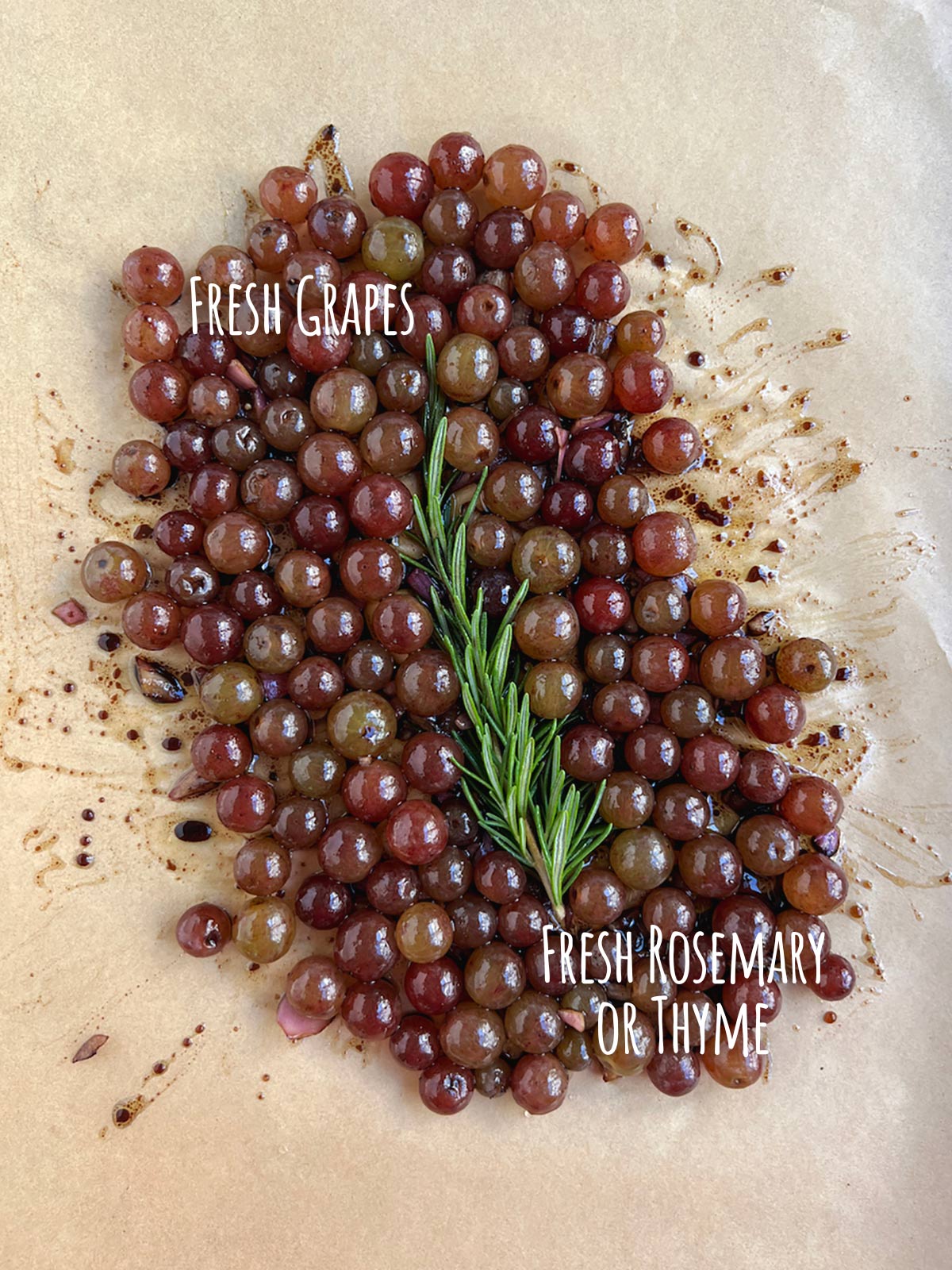Ingredient shot for baked grapes showing fresh grapes and fresh rosemary on parchment paper.