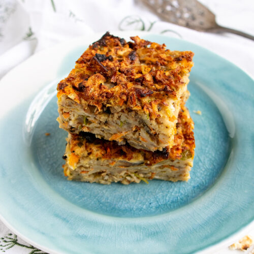 Two slices of savory matzo farfel kugel on a blue plate with a server in the background.