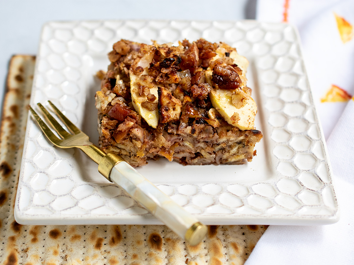 Apple matzo kugel on a white plate with a gold fork and sitting atop matzo boards!