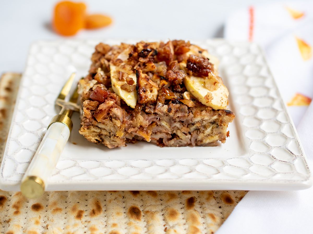 Close up side view of apricot matzo kugel on a white plate with dried apricots in the background.