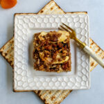 Apple Matzo Kugel on a white plate with a board of matzo in the background.