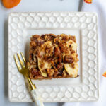 Top down view of a piece of apple matzo kugel on a white plate with apricots and matzo in the background.