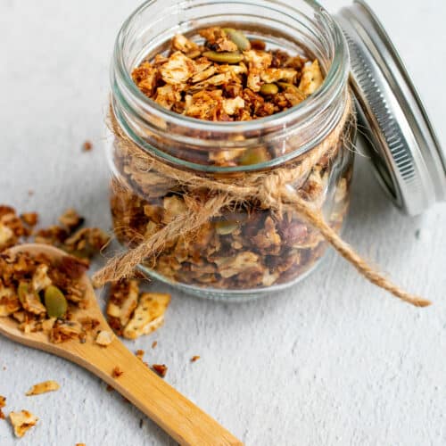 Matzo granola in a small canning jar with a decorative string and a wooden spoon of granola on the side.