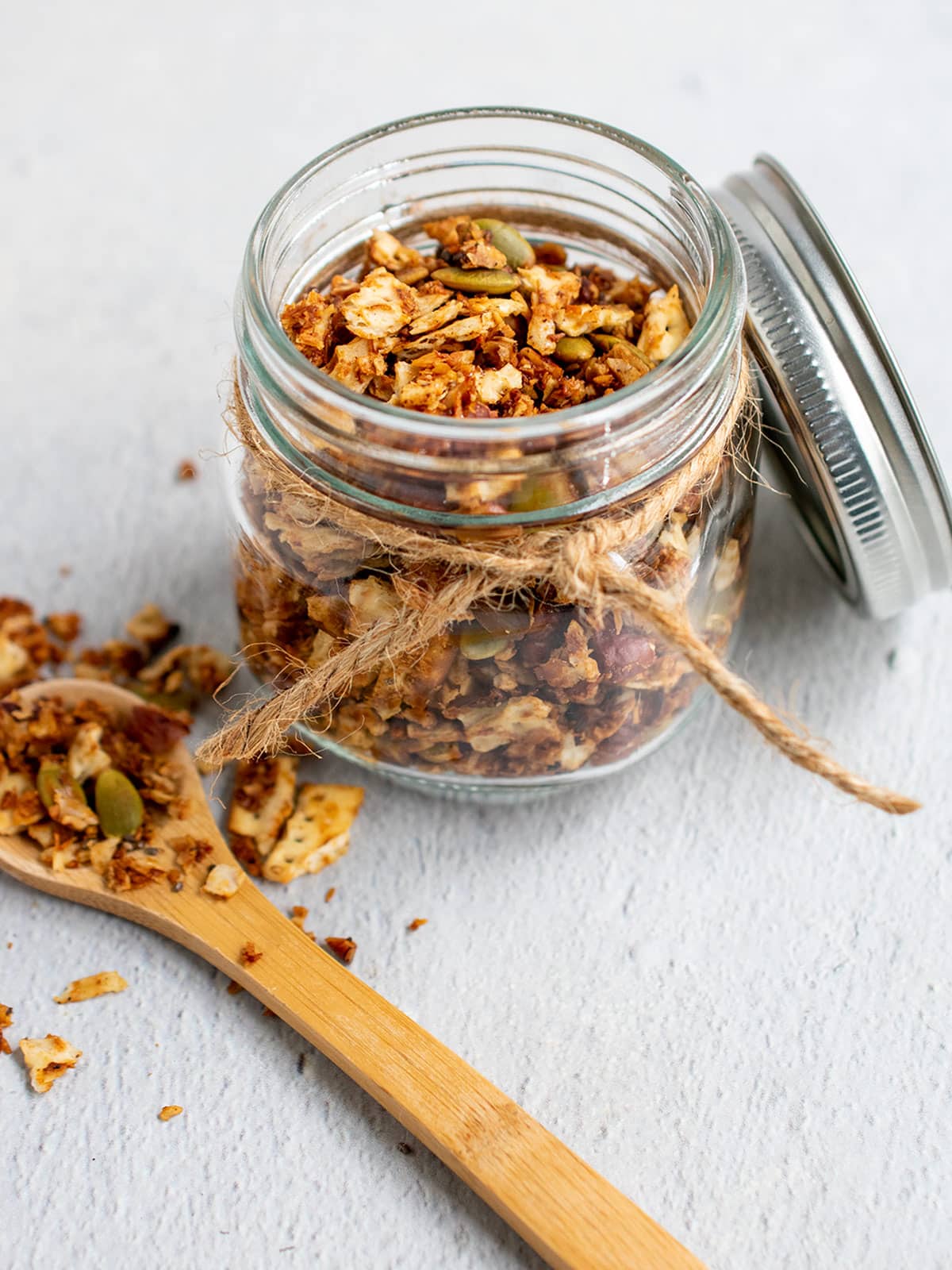 Matzo granola in a small canning jar with a decorative string and a wooden spoon of granola on the side.