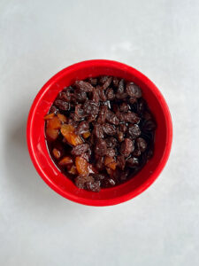 Raisins and apricots soaking in hot liquid in a red bowl.