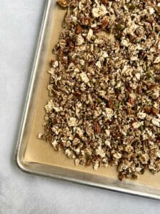 Uncooked granola on a parchment-lined baking sheets ready to go in the oven.