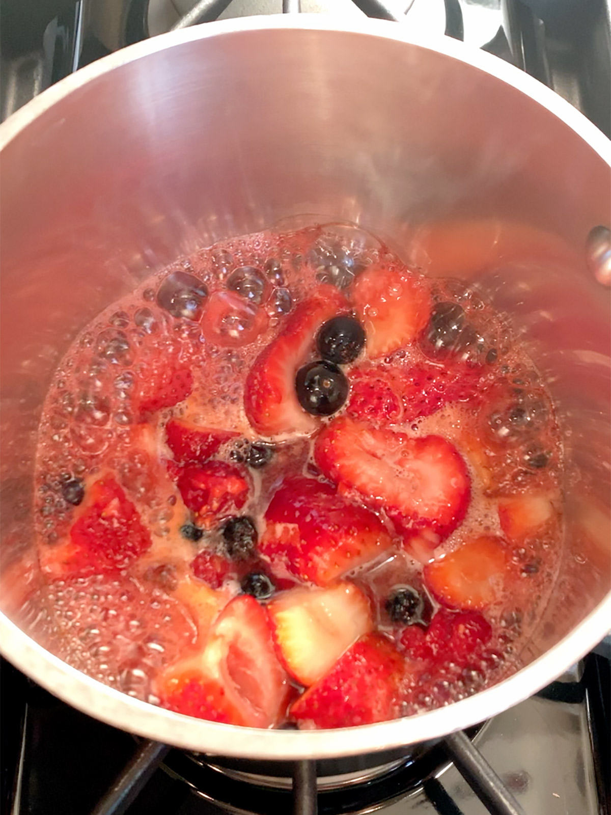 Berry compote boiling in the pot on the stove.