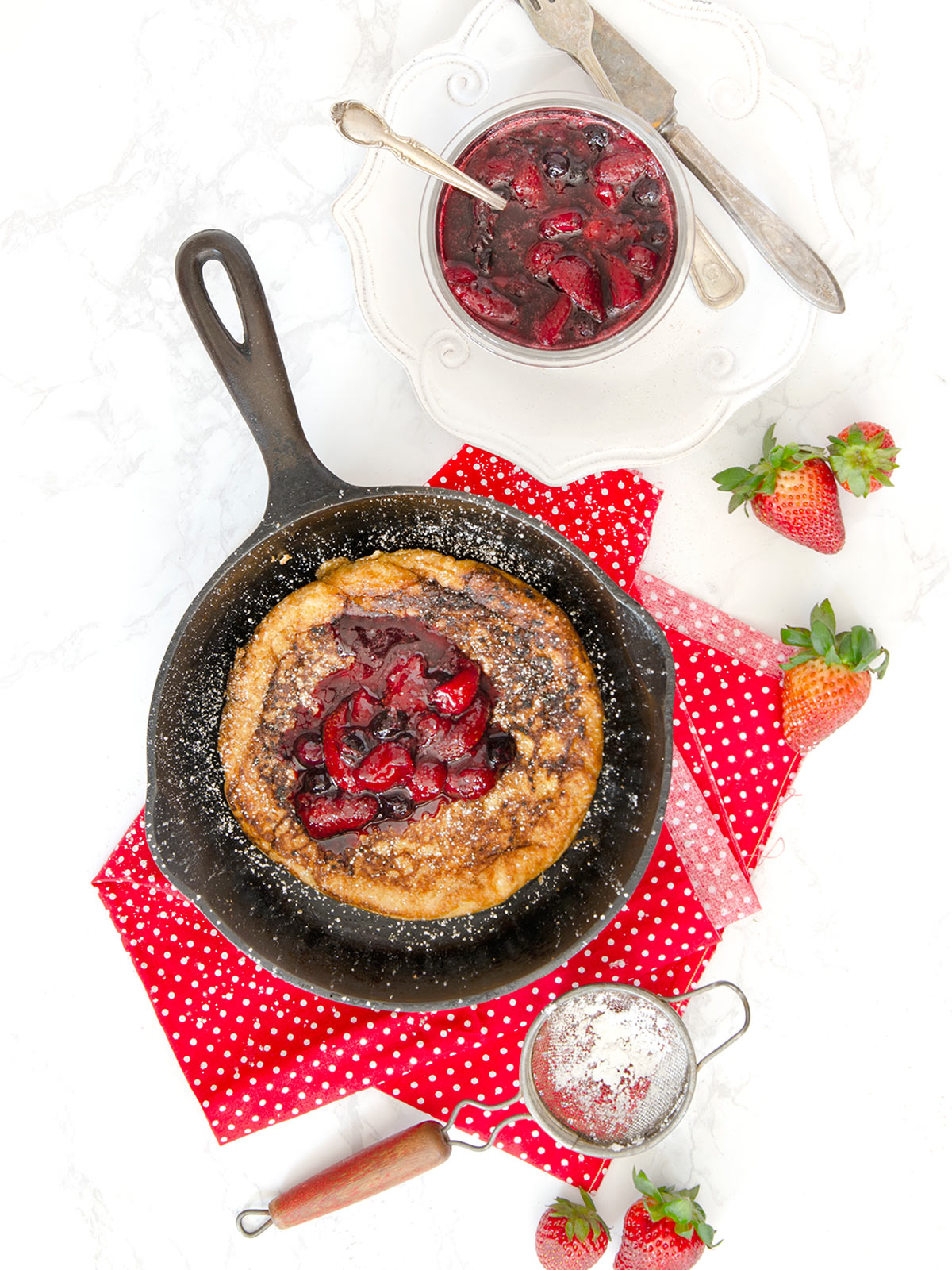 Matzo meal pancake in a cast iron pan with fruit compote on top and on the side in a clear glass bowl.