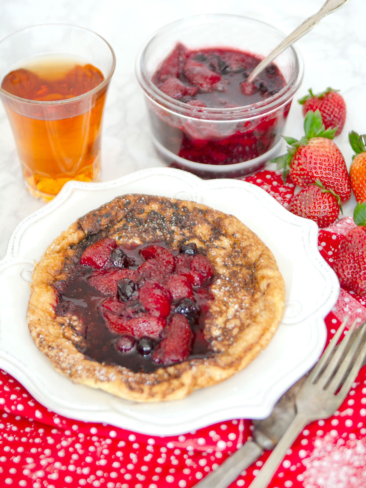 Berry fruit compote spooned on pancake with extra in a glass bowl in the background.