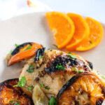 Pinterest image showing chicken on a tan plate with slices of clementines.