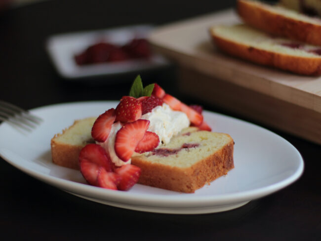 landscape image beauty shot of loaf with whipped cream and strawberries on it.