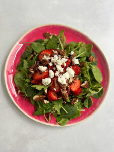 Goat cheese, pecans, strawberries and spinach on a pink plate.