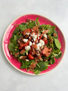 Strawberry goat cheese salad on a pink plate with strawberry balsamic dressing.