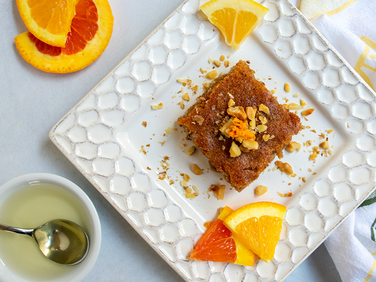 Slice of tishpishti cake on a square plate topped with nuts and orange zest.
