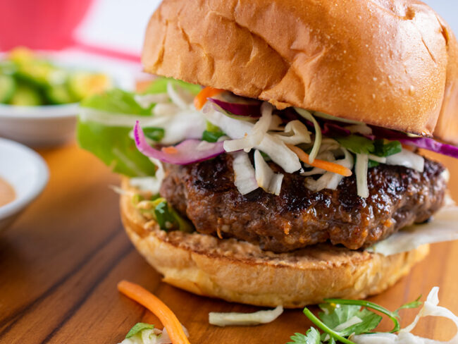 Beauty shot of burger on a wooden border with coleslaw tucked into the bun.