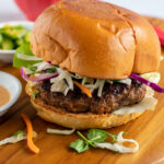 Bulgogi burger on a wooden board with a red bowl of coleslaw in the background.