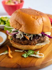 Bulgogi burger on a wooden board with a red bowl of coleslaw in the background.