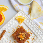 Pinterest image showing honey almond cake on a white plate with citrus decoration.