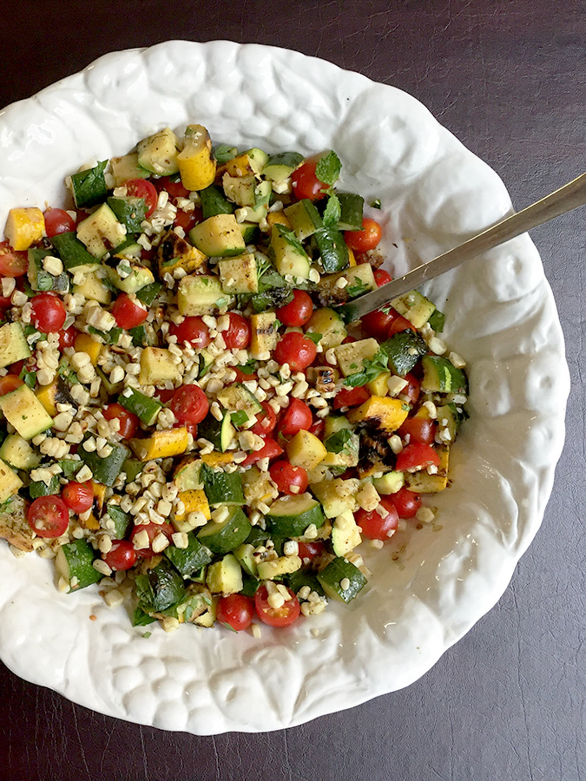 Corn salad in a big white bowl with a serving spoon in the bowl.