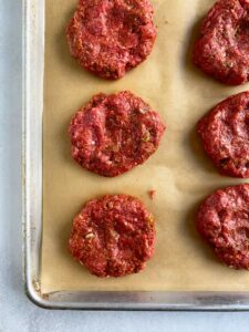 Formed burger patties on a parchment paper on a sheet tray.