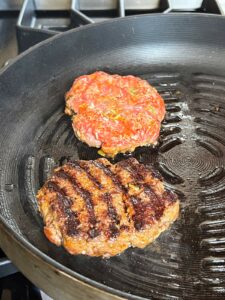 Two bulgogi burger patties on an indoor grill pan with one turned over and one not turned over.