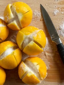 Fresh lemons cut and filled with salt on a wooden cutting board with a knife next to it.