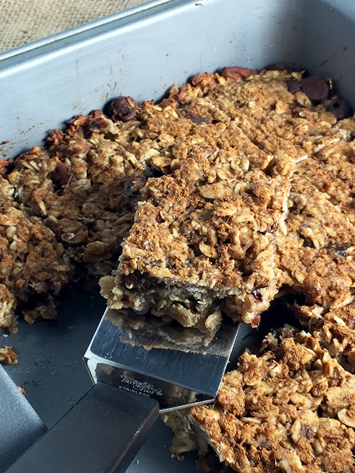 Banana oat bars in grey pan with a small spatual holding one.