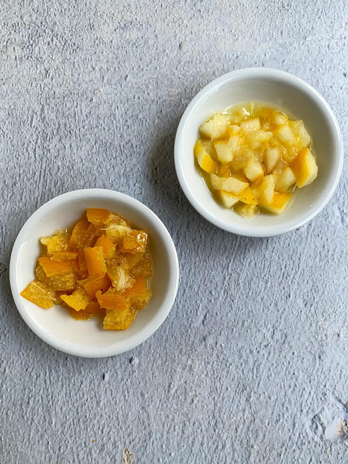 Two small white bowls with regular preserved lemons in one and quick pickled lemons in the other.