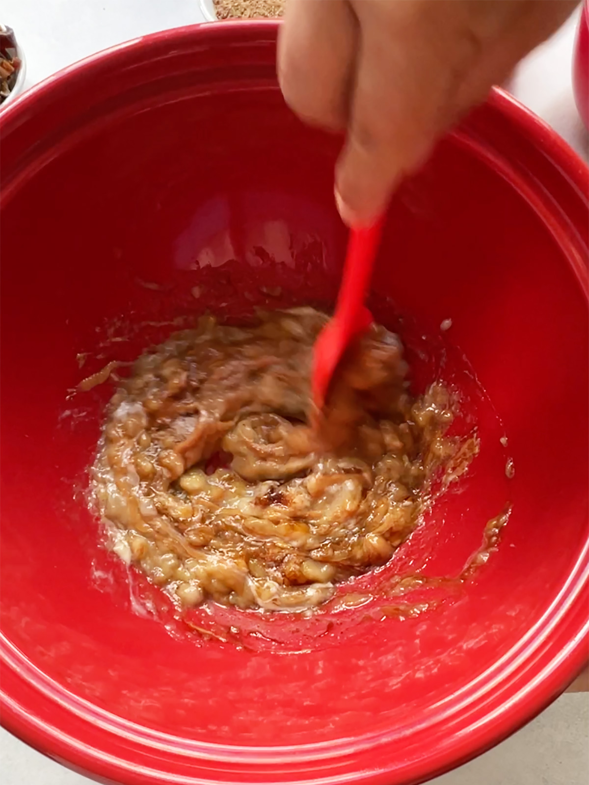 Mixing wet ingredients for banana oat bars in large red bowl with a red spoon.