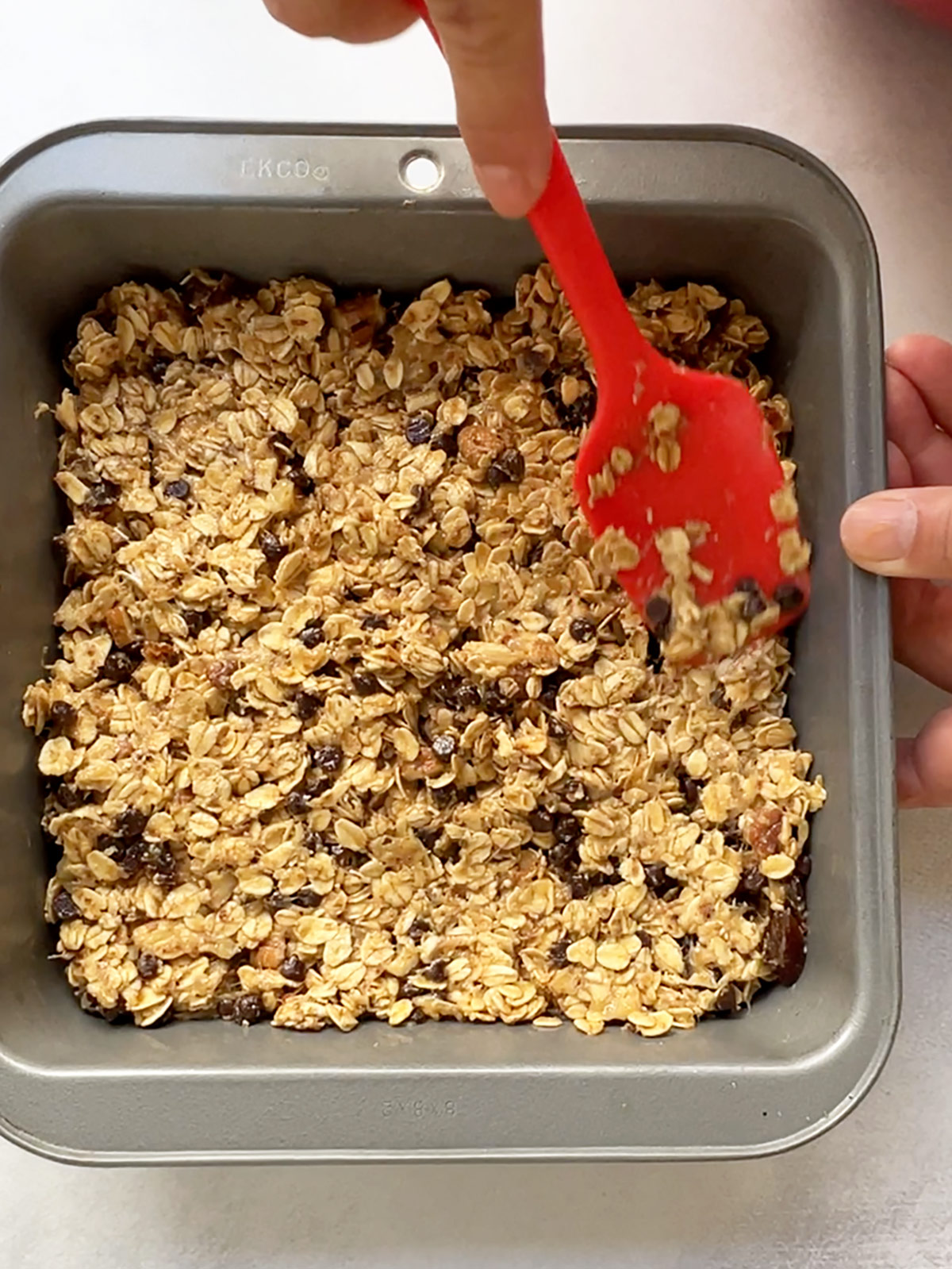 Peanut butter banana oat bars being spread in a grey square baking pan with a red spatula.