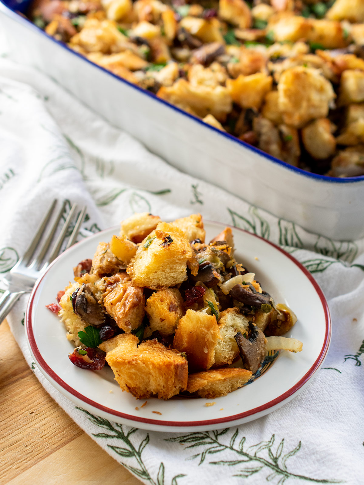 Mushroom challah stuffing on a small plate with a fork with the large casserole in the background.
