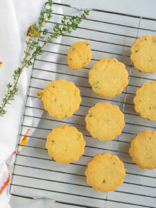 Cocktail cookies on a cooling rack with fresh thyme and a napkin to the left.
