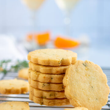 Stack of orange shortbread cookies of different sizes with cocktails in the background.
