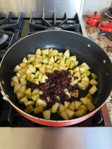 Dried cranberries added to apples in large pan.