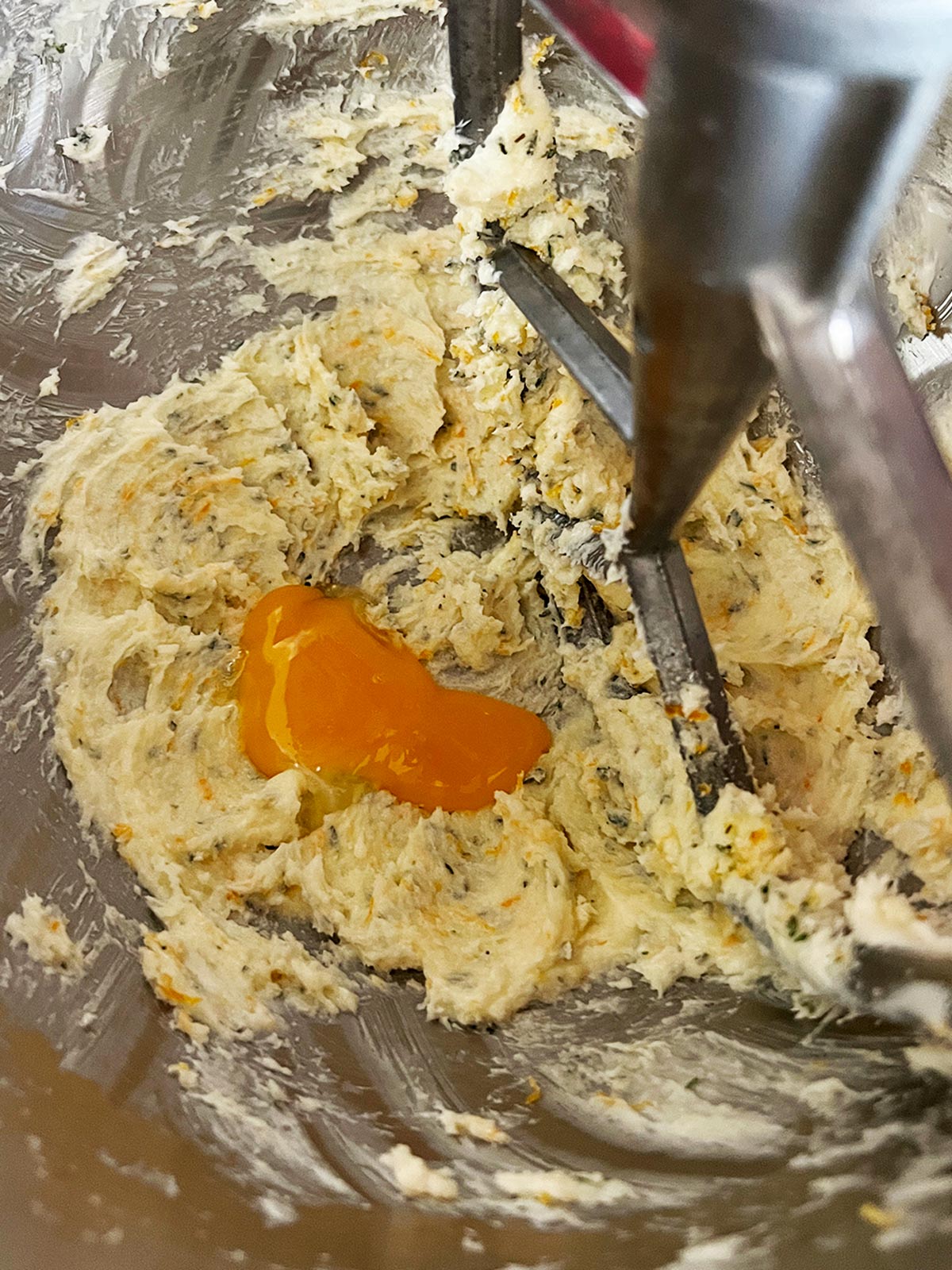 Adding egg yolk to creamed butter sugar mixture in mixing bowl.