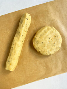 Orange shortbread cookie dough on a piece of parchment paper. Half of the sablé-like dough is pressed into a disk and half is rolled into a log.