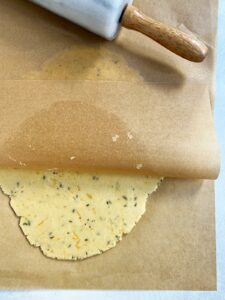 Orange shortbread dough rolled out between two pieces of parchment paper.