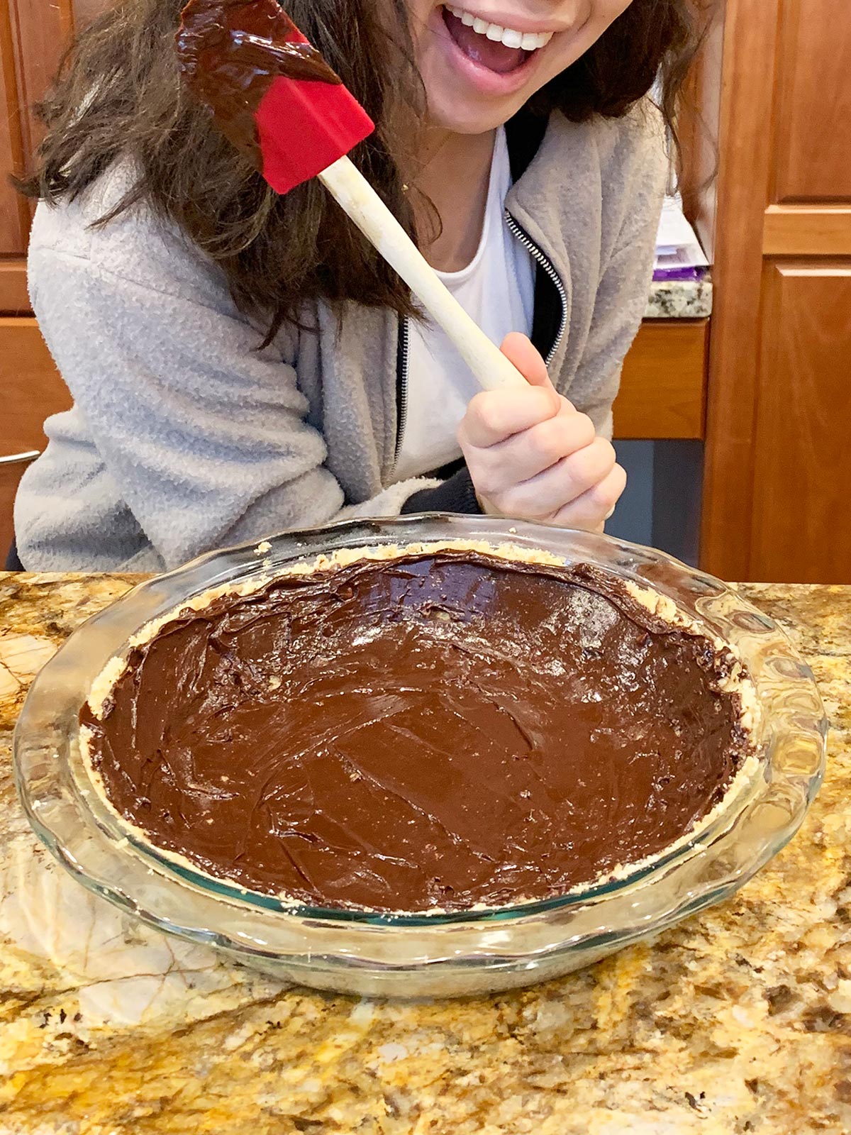 Beth's daughter holding a red spatula after she spread the chocolate lining on the cooled crust.