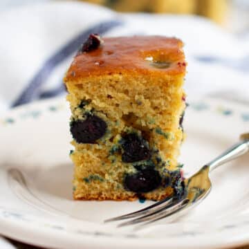Close up of one slice of blueberry cake with a fork and more slices of the cake in the background.