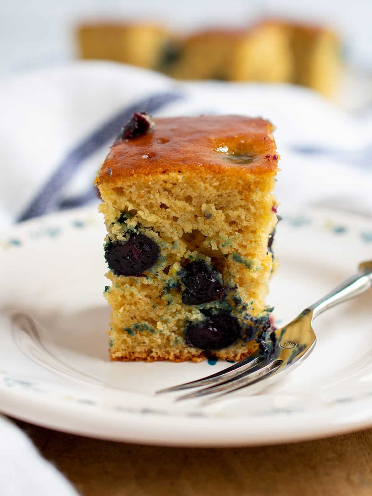 Close up of one slice of blueberry cake with a fork and more slices of the cake in the background.