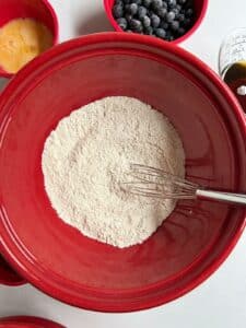 Dry ingredients in a big red bowl with a small whisk.