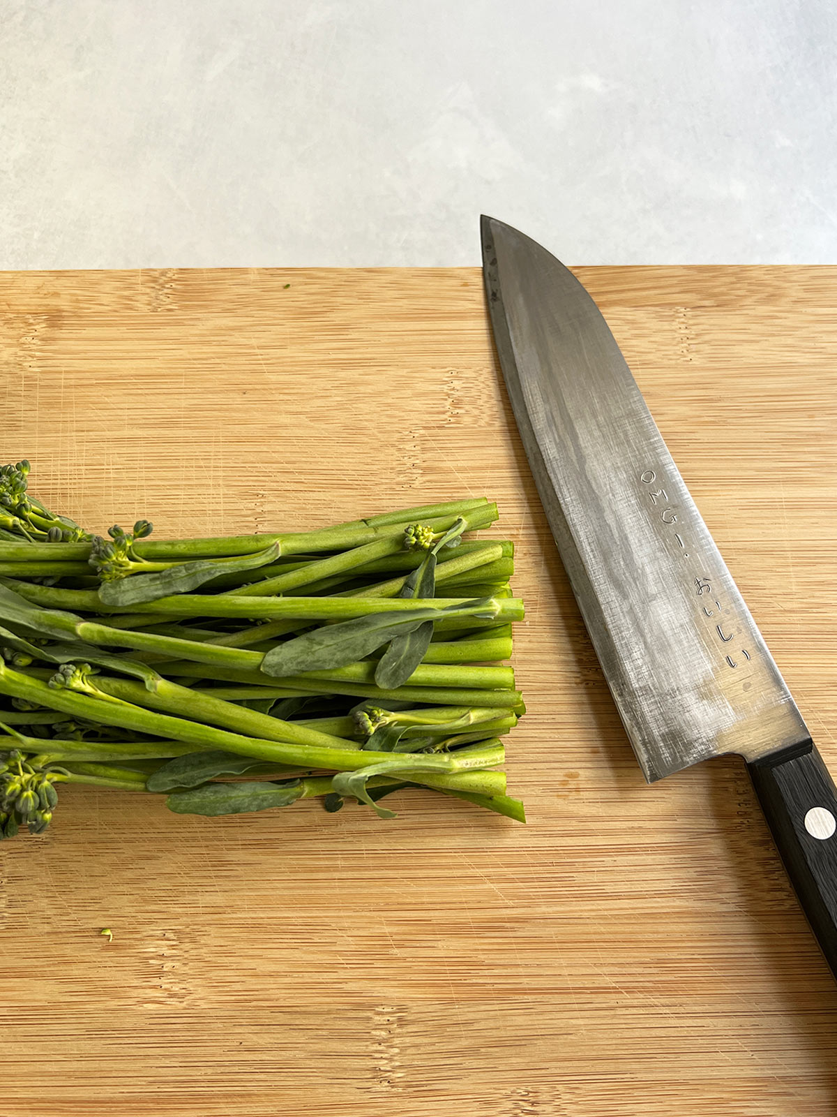 Broccolini on a wooden cutting board with a Japanese knife to cut the stalk ends.