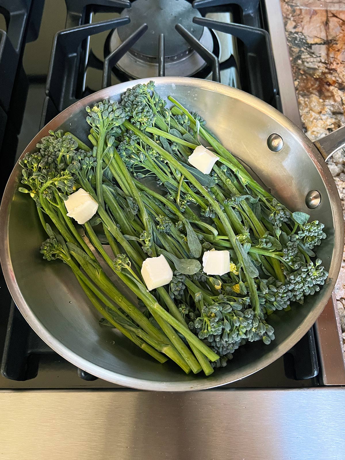 Baby broccoli in a sauté pan with cubes of butter.