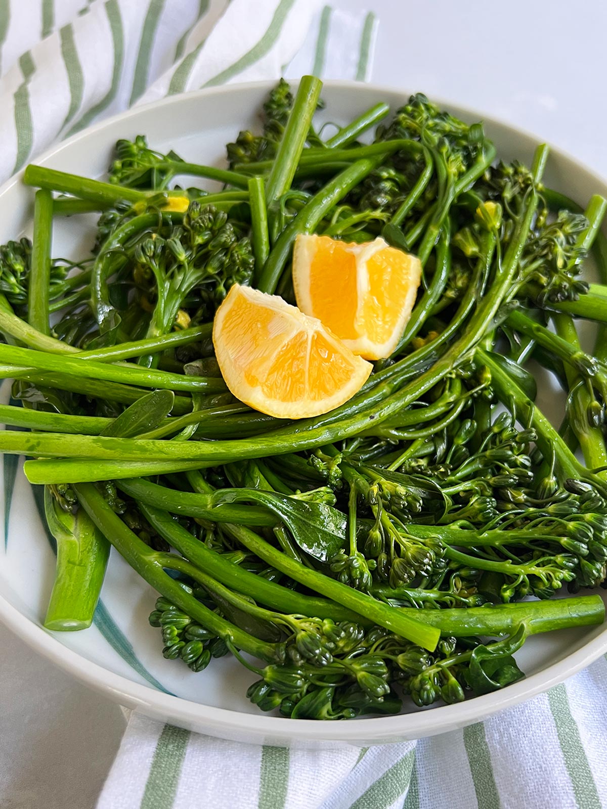 Angle view of plated broccolini with a striped napkin underneath.