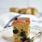 Pinterest image showing one slice of the blueberry breakfast cake on a small plate with several more slices in the background.