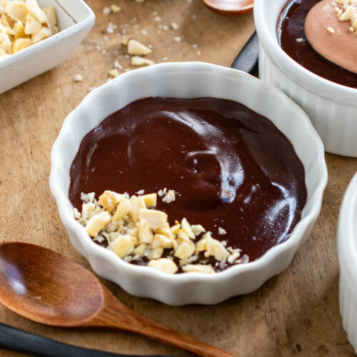 Dairy free chocolate pudding with nuts on top and other bowls of pudding with whipped cream in the background.