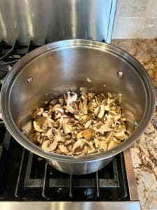 Fresh and dried mushrooms added to mushroom barley soup in soup pot.