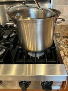 Side view of the soup pot on the stove with lid partially on while it cooks.