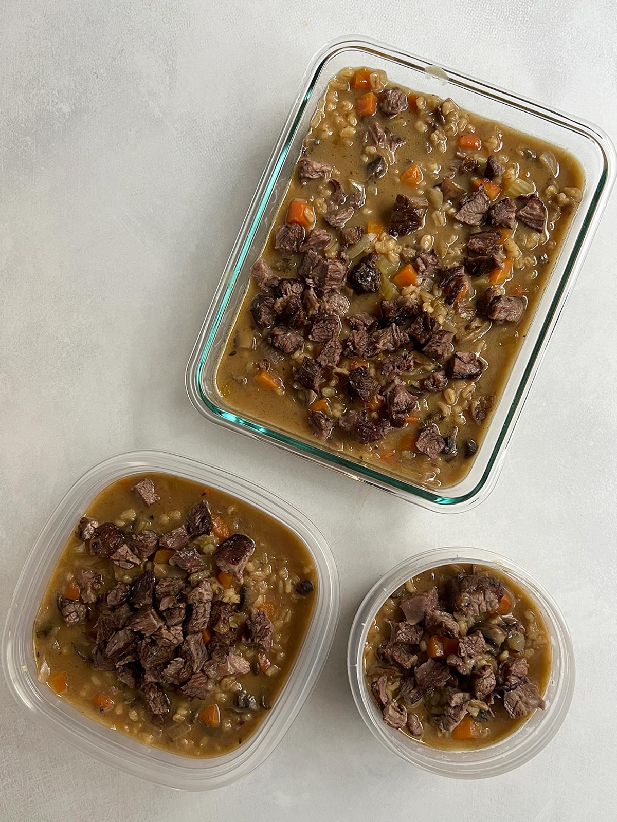 Beef mushroom barley soup in containers with meat added and ready to refrigerate.