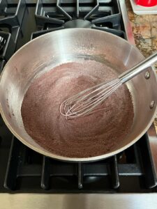 Sifted dry ingredients for dairy free chocolate pudding in the pot with the whisk.